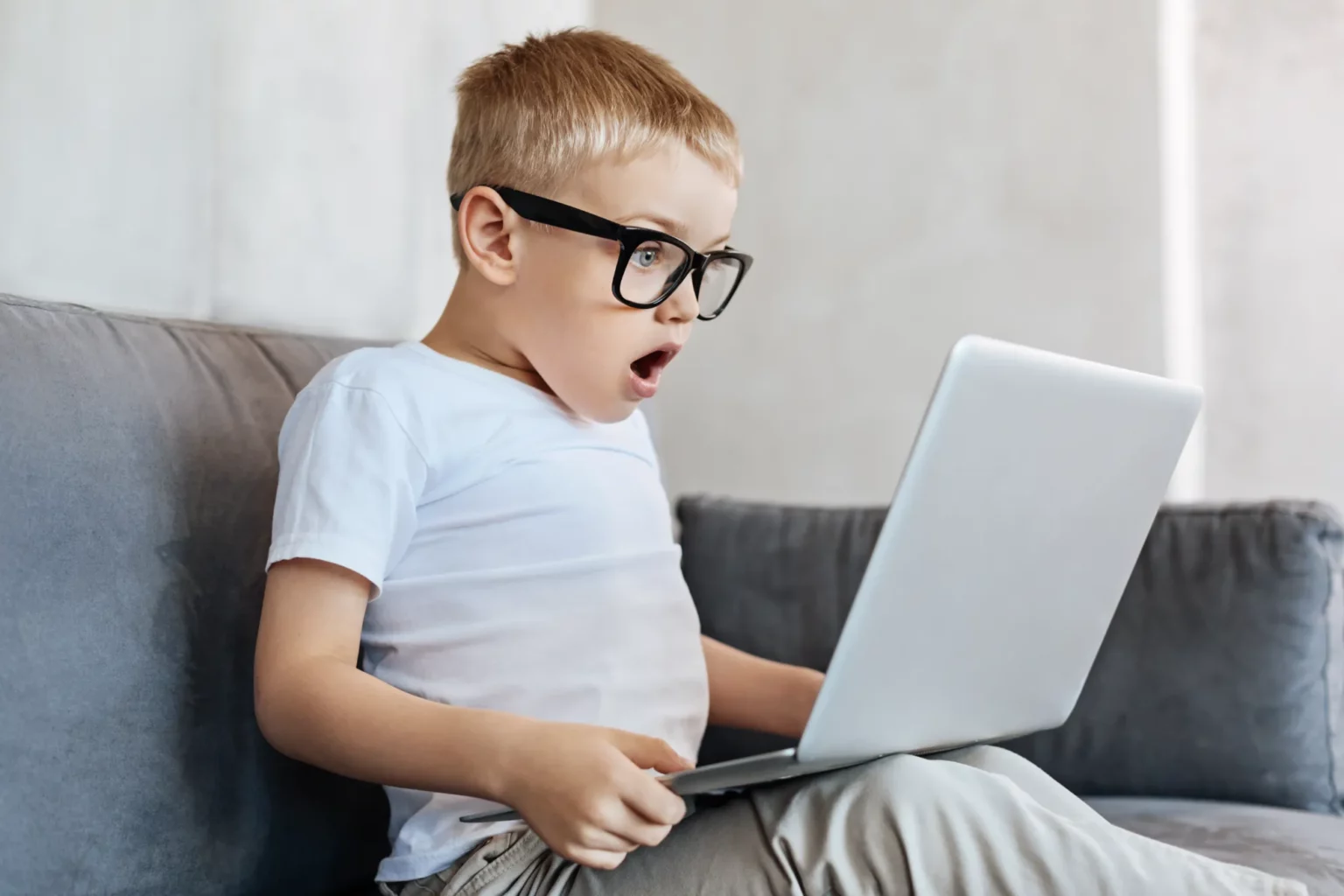 zdziwiony chłopiec siedzący na kanapie przegląda strony internetowe