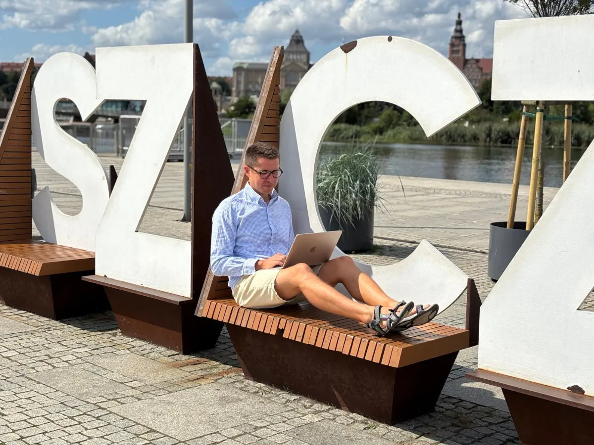 krzysztof kwaśniowski właściciel enjoy ads studio siedzący na ławce przed dużym napisem szczecin